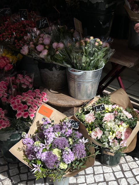 A display of fresh floral arrangements and bouquets at a flower shop, featuring a variety of flowers including pink roses, purple alliums, and white blooms, arranged in wrapped bouquets and metal buck