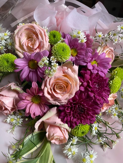 A vibrant floral arrangement featuring soft pink roses with tightly curled petals, complemented by bright purple daisy-like flowers with yellow centers, and striking green chrysanthemums with densely 